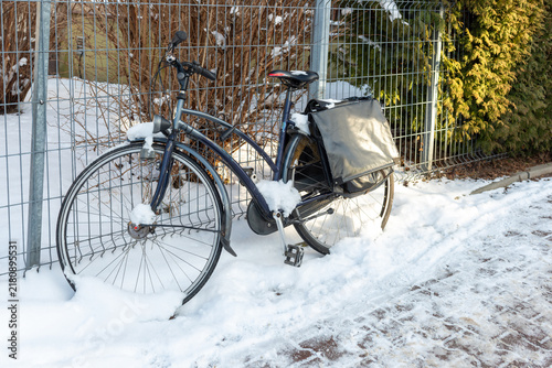 Bild auf Leinwand Dark city bicycle with large rear pannier stands beside a metal fence surrounded by fresh snow