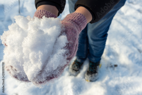 Obraz na płótnie Close-up of a person holding a handful of fresh sparkling snow in warm knitted mittens outdoors