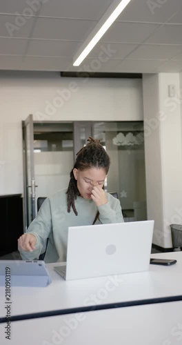 Vertical video: Nonbinary rubbing eyes taking glasses donning for focus typing on laptop at desk