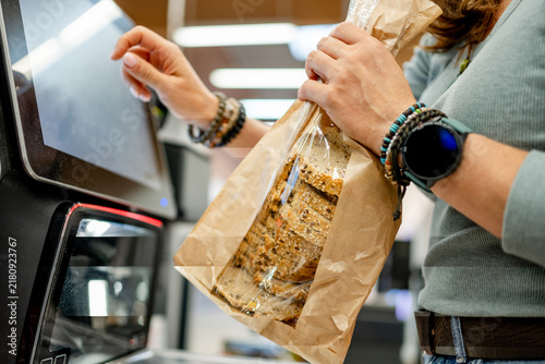 Foto Woman scans fresh loaf of multigrain bread at automated grocery store checkout s