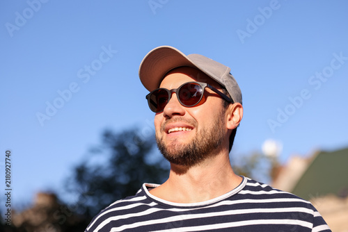 Happy man wearing stylish sunglasses and cap against blue sky, low angle view. Space for text