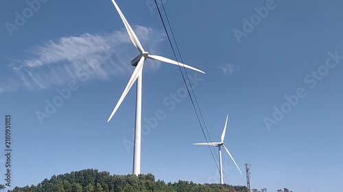 White wind turbines rise majestically above a green forest under a clear blue sky, symbolizing clean, renewable energy. Perfect for ecological and sustainability concepts. Nobody.