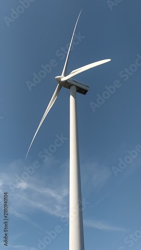 This towering white wind turbine stands majestically against a bright blue sky, symbolizing clean energy, hope, and sustainability for a greener future. Low angle view, nobody.