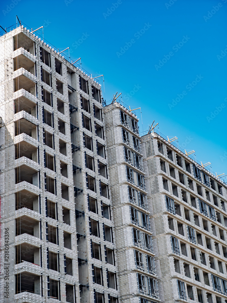 Fototapeta premium Unfinished modern high-rise building under construction against clear blue sky