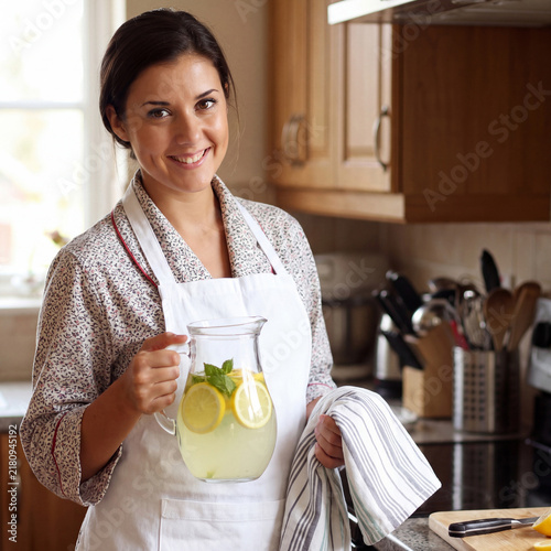 Happy housewife in an apron holding homemade lemonade in a jug