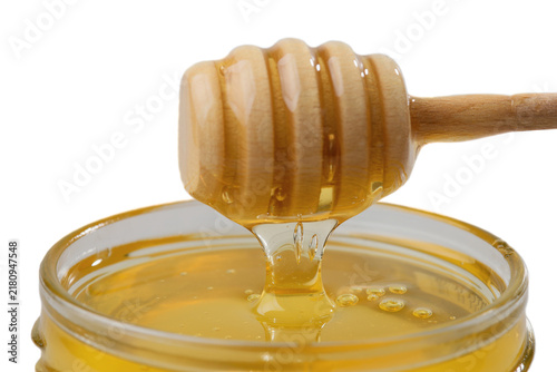 Linden honey dripping from wooden spoon into glass jar on white background.