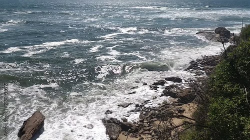 With nobody in sight, wild ocean waves crash powerfully against a rocky, sunlit coastline, evoking a deep feeling of raw natural strength, untamed energy, and serene freedom.