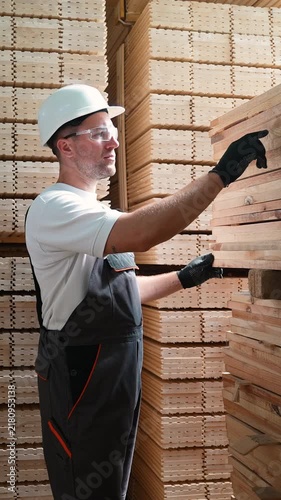 Warehouse worker inspecting and counting stacked wooden planks