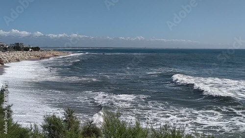 A majestic shot of powerful ocean waves crashing onto a sandy coast under a clear blue sky, evoking a sense of peaceful freedom. Nobody in sight. Perfect for travel and nature themes.