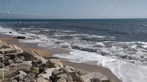 Experience natures power with waves crashing on a sandy shore and rugged rocks. This peaceful, sunny coastal landscape evokes a sense of escape and serenity. Nobody is present.