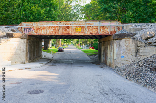 фотографія Low clearance rusty railroad bridge spans a quiet tree-lined suburban street