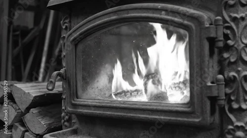 Black and white close up of a vintage wood-burning stove with flames and firewood for warmth and ambiance