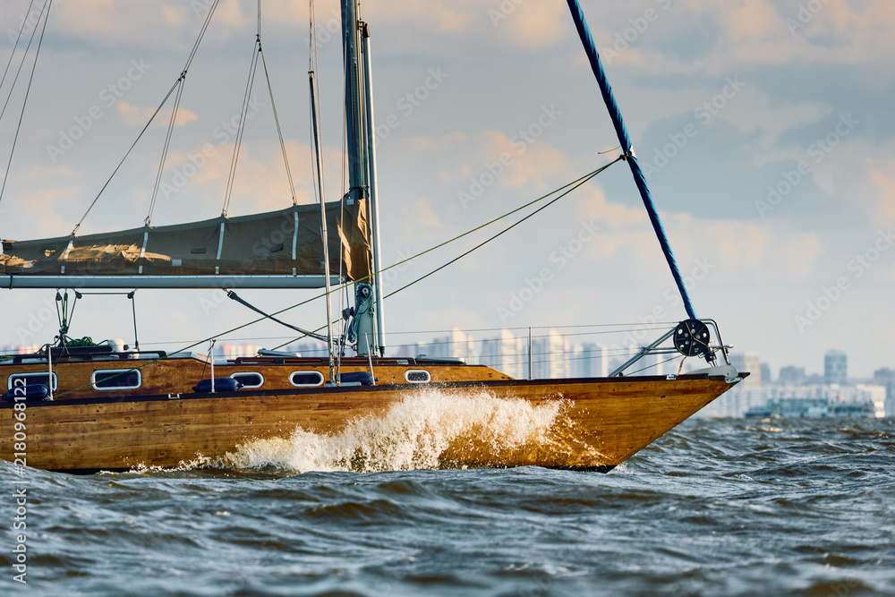 Obraz premium Vintage sailing boat through splashing water at sunset, Sailing regatta in the Gulf of Finland at sunset, hot race of several yachts, teamwork
