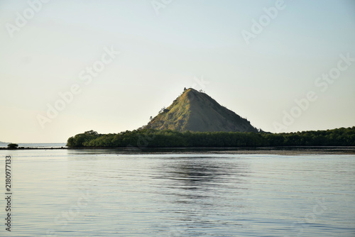 Sailing to Komodo Island in clear weather, passing rugged hills amidst the crystal-clear waters of Rinca Island, Labuan Bajo, Indonesia.