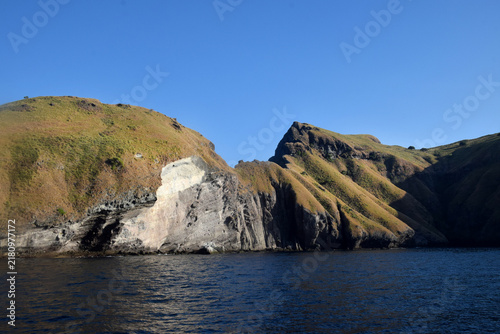 Sailing to Komodo Island in clear weather, passing rugged hills amidst the crystal-clear waters of Rinca Island, Labuan Bajo, Indonesia.