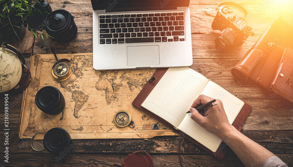 Obraz premium A traveler plans an adventure on a vintage world map, using a laptop, compass, and camera. This rustic desk scene evokes feelings of wanderlust, discovery, and creative freedom for any journey.