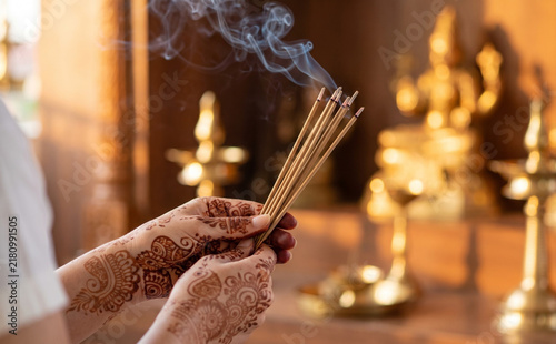 Young Indian woman holding burning incense sticks with traditional mehndi henna tattoos for prayer ritual
