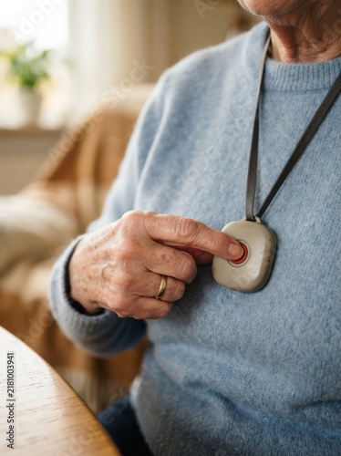 Elderly woman pressing emergency panic button pendant device around her neck for senior safety