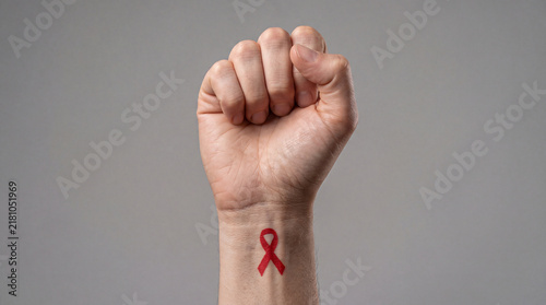 A close-up of a person's clenched fist with a red ribbon symbol painted on the wrist, representing support for HIV and AIDS awareness and health advocacy.