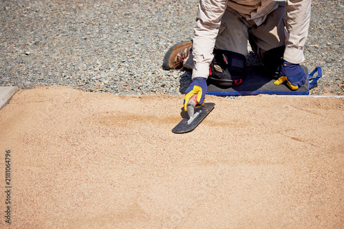 Man using a trowel to smooth sand in preparation for laying patio blocks