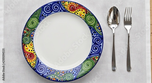 Empty decorative plate and silverware rest on a white placemat