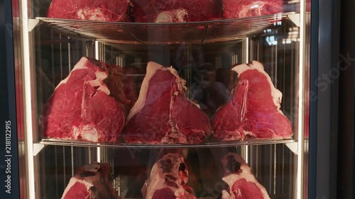 Close up shot of premium dry aged T-bone beef steaks inside glass display fridge at butcher shop.