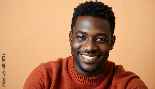 Portrait of a smiling young Black man wearing a warm orange sweater against beige background