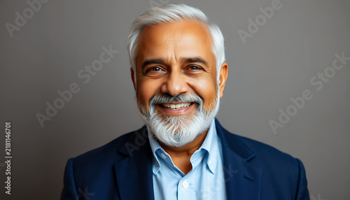 Portrait of a smiling mature Indian businessman in a blue blazer against grey background