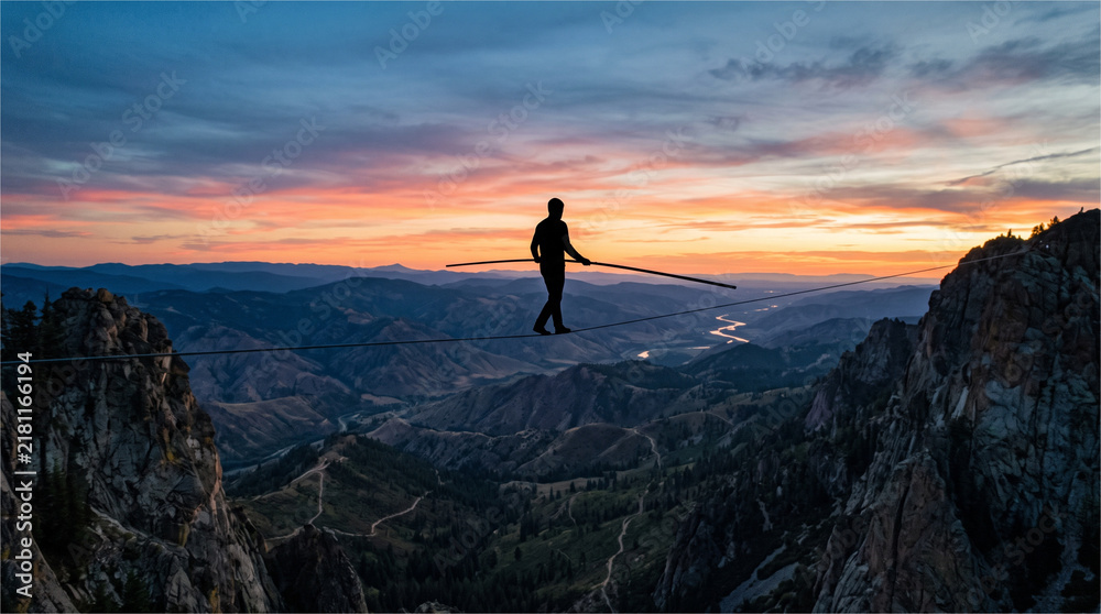 Fototapeta premium Silhouette of Person Highlining Across Mountain Canyon at Sunset
