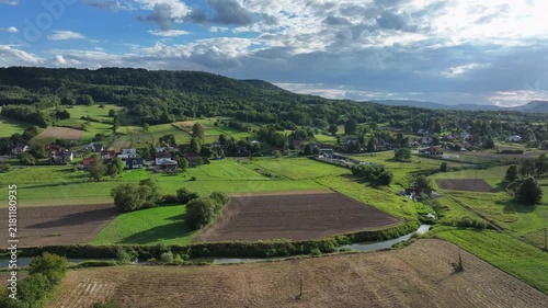 Aerial valley village farm river southern Poland. South eastern Poland. Historic mountain valley village with 15th century wooden All Saints Church. Agriculture land, rivers, forest and rural farm.
