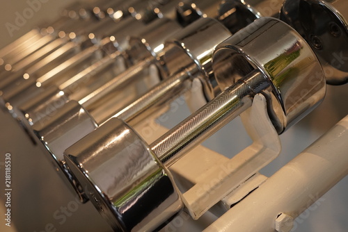 Konstfotografi Rows of chrome dumbbells on a white storage rack in a modern home gym corner