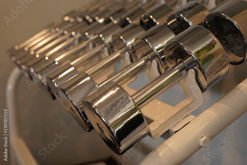 Konstfotografi Rows of chrome dumbbells on a white storage rack in a modern home gym corner