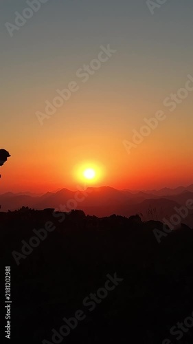 Alpinista con mochila de trekking ascendiendo por la cima de una montaña al atardecer con el sol detrás, luz dorada intensa y una vista panorámica épica del horizonte
