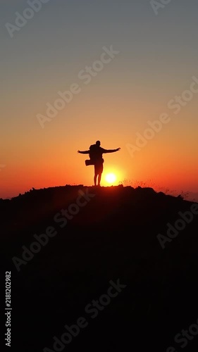 Alpinista con mochila de trekking ascendiendo por la cima de una montaña al atardecer con el sol detrás, luz dorada intensa y una vista panorámica épica del horizonte