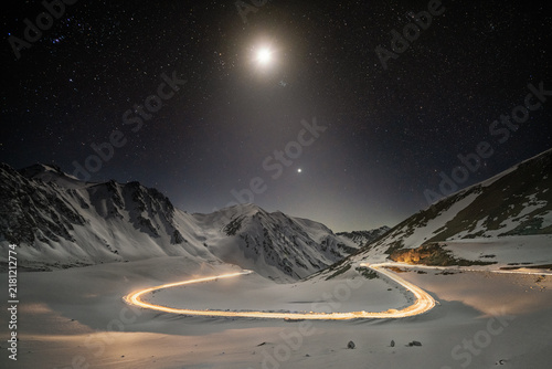 Moonlit Mountain Road with Light Trails in Snow-Covered Tien Shan Mountains