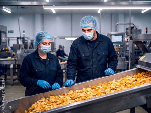 Factory Workers Inspecting Potato Chips on Conveyor Belt in Food Processing Plant