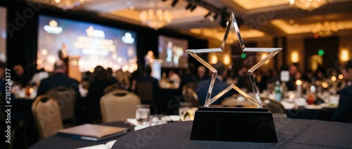 Star-shaped award on a table at a corporate event with a blurred audience and stage in the background.