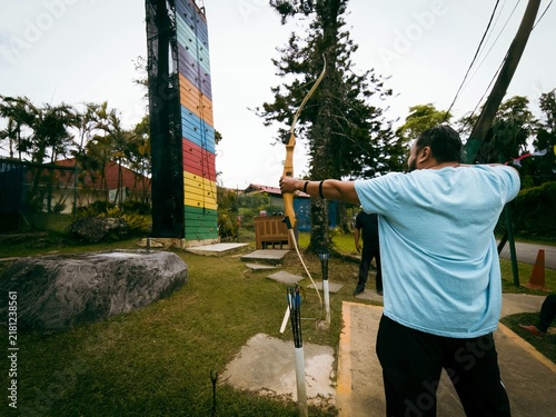 A man is firmly pulling the string of a big bow in an extreme park.