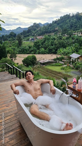 Canvastavla Relaxed man soaking in outdoor bubble tub surrounded by tropical nature and moun