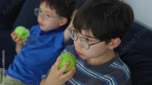 cute young boy with glasses eating a fresh green apple. Healthy childhood nutrition, daily vitamin snack, and casual indoor lifestyle portrait of a kid enjoying organic fruit.