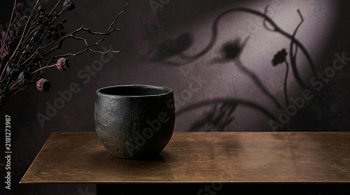 Dark handcrafted ceramic bowl on a wooden table with floral shadows in the background still life floral shadow home decor pottery art black bowl fine art