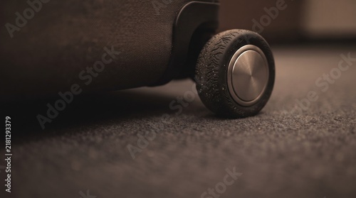 A suitcase wheel with worn tread rests gently on dark, plush carpeting. The atmosphere suggests a traveler pausing momentarily in a warm hotel room, ready for adventure.