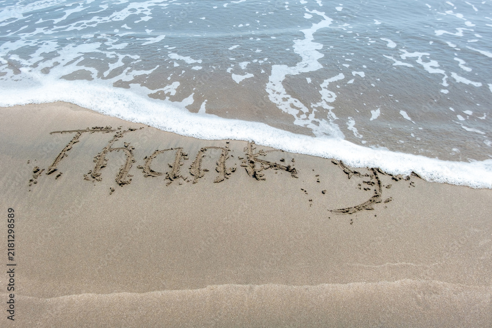 Fototapeta premium Thanks handwritten on sand with ocean water wave background.