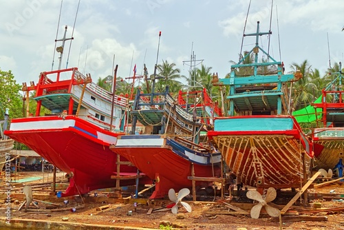 Traditional colorful wooden Thai fishing boats undergoing maintenance and repairs on dry land along the coast in Sichon, Nakhon Si Thammarat province, Thailand.