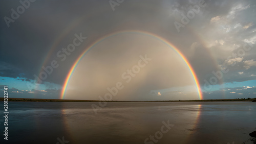 Vibrant double rainbow over a flat open landscape under cloudy sky
