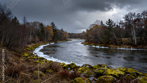 Misty river flowing through autumn forest under dark clouds