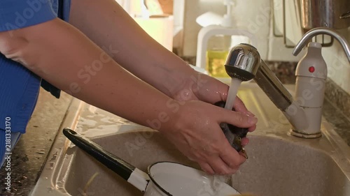 Person rinses dark olives under running water at kitchen sink, demonstrating food preparation, clean produce handling, handheld camera captures detailed action.