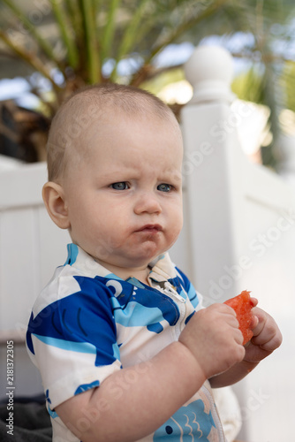 Baby boy with watermelon on his face wearing a shark-themed swimsuit
