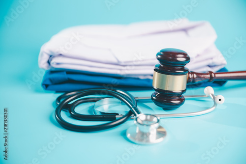 Fotografie Judge gavel and stethoscope beside folded medical uniforms on a blue background