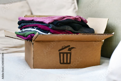 Фотография Box with folded clothes marked with trash bin icon as concept for textile waste